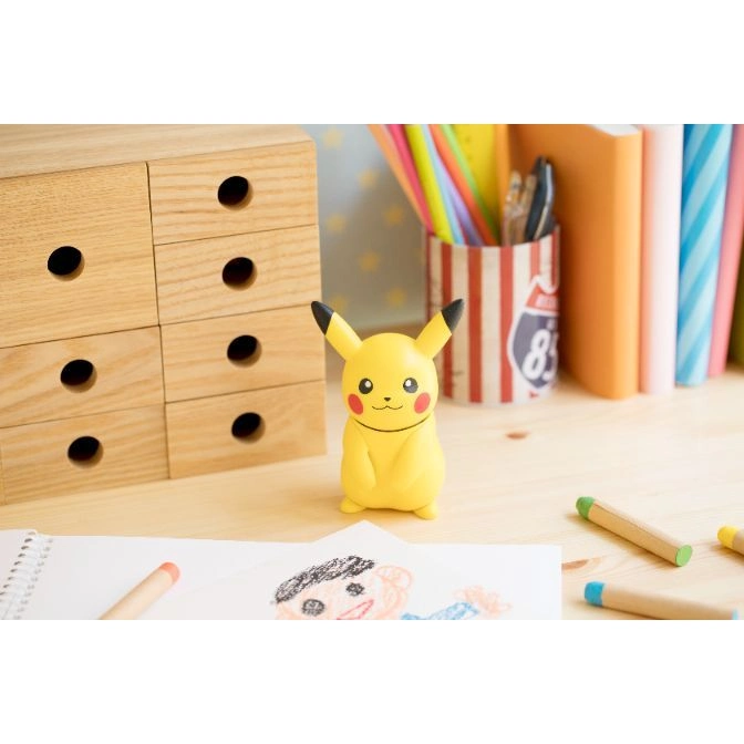  Pikachu toy figure with black-tipped ears, red cheeks, and a smiling face on a desk with art supplies.