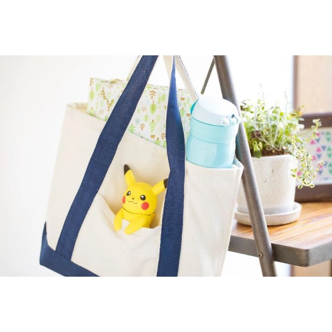  Pikachu toy in a tote bag pocket. Yellow body, black ears, red cheeks, and smiling face.