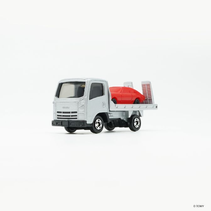  Silver Isuzu truck carrying a red toy car on its flatbed.